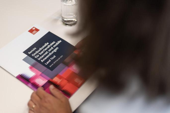 © Land Tirol/Simon Rainer Bericht der Ombudsstelle für barrierefreies Internet liegt in der Druckversion auf dem Tisch und wird von einer Frau die man von hinten sieht betrachtet